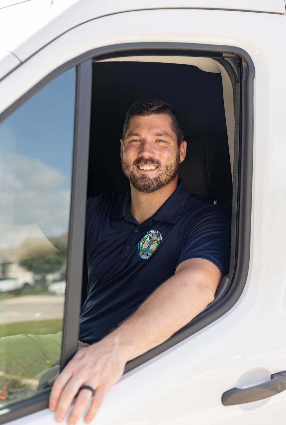 Man smiling from the driver's seat of a van, wearing a blue shirt with a logo.